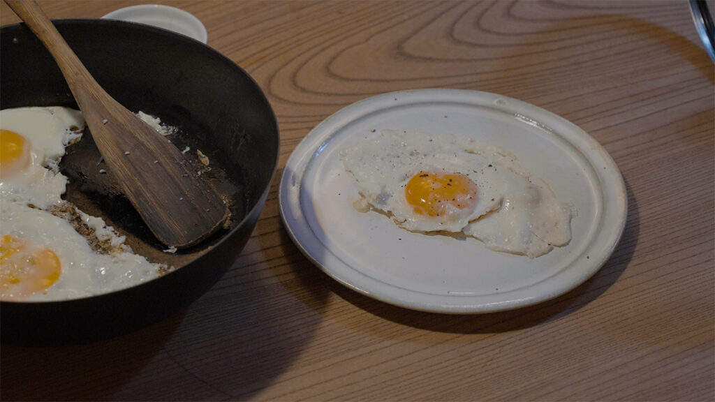 卓上に置かれたVERMICULARの24cm深型フライパンで焼いた目玉焼きを皿に盛り付けした様子。ふっくらと焼き上がった卵が朝の食卓を温かく彩る。