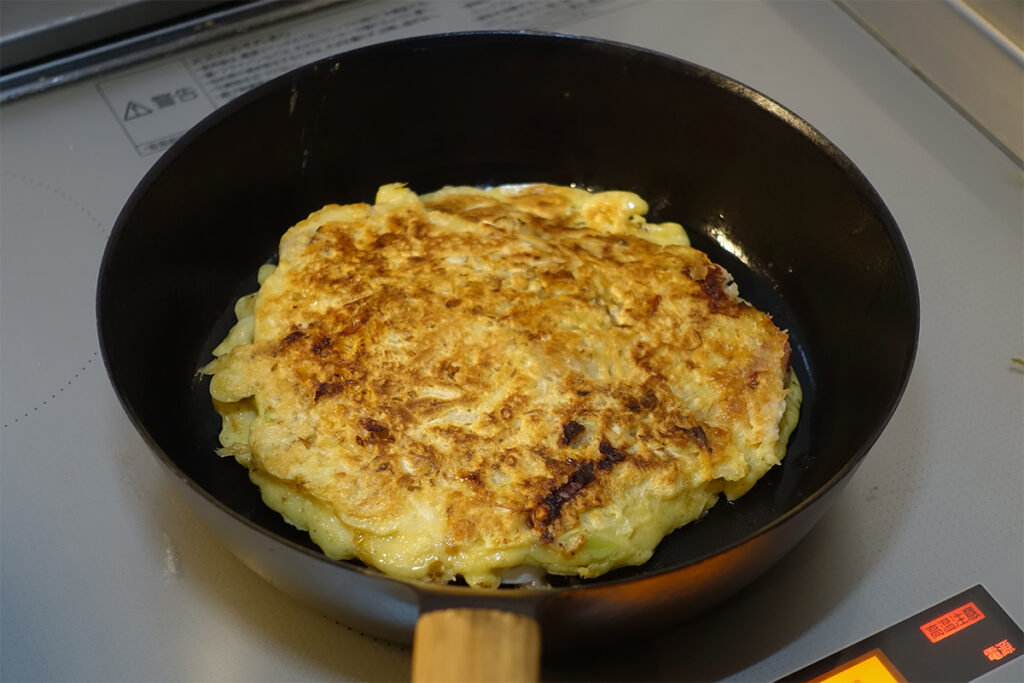 VERMICULARの24cm深型フライパンでお好み焼きを焼いている様子。ふっくらと生地が膨らみ、香ばしい香りが立ちのぼる。
