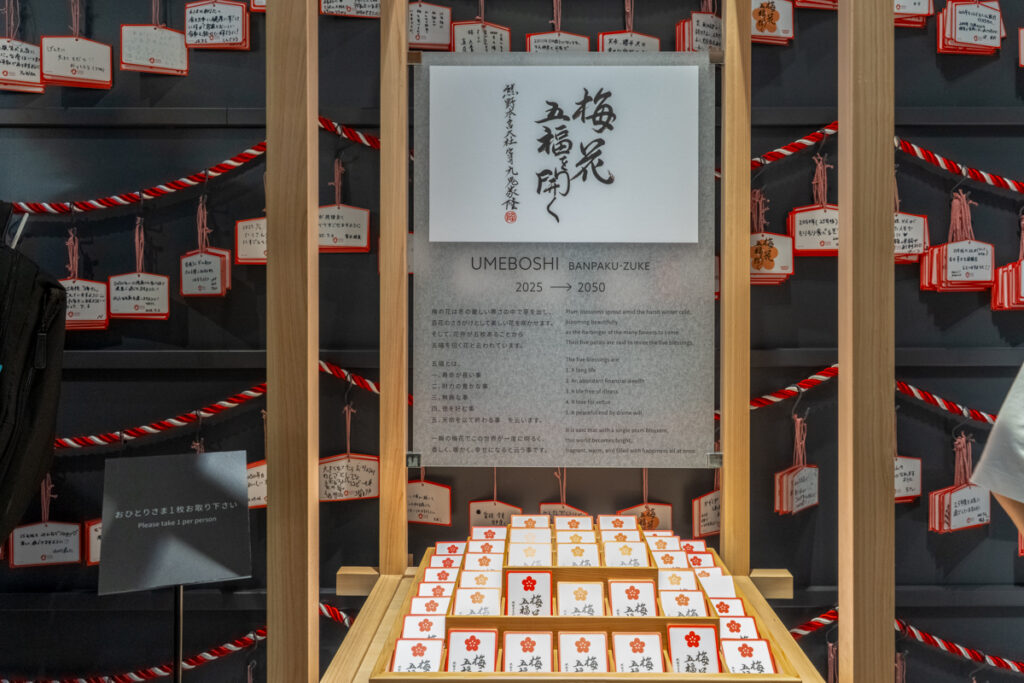 EARTHMARTの未来フロア展示。壁に飾られた絵馬の手前に万博漬け引換券が置かれ、来場者は一人一枚ずつ受け取れる様子