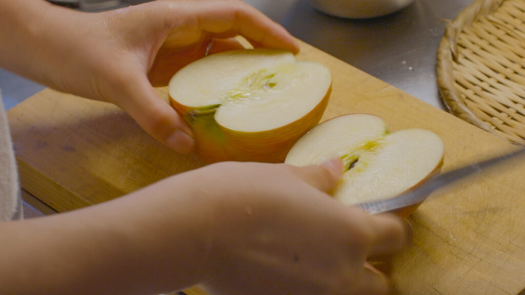 まな板の上でリンゴを包丁で切る手元。赤い果実の瑞々しさと、日常の食卓に秋の実りが還る瞬間