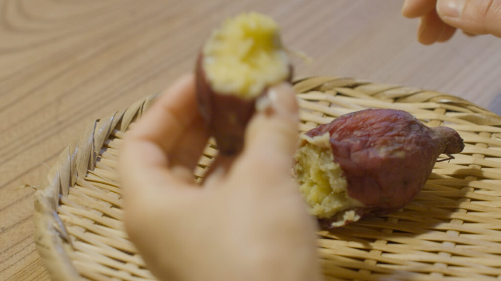 ストーブで焼いた焼き芋を手に持ち、ほくほくとした中身を味わっている様子を手元のアップで写した写真