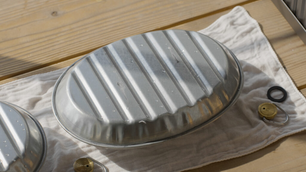 使用後のマルカの金属製湯たんぽの水を流し、ベランダで逆さにして乾かしている様子。日光や風にあてて水気を飛ばし、清潔に保つ工程がわかるシーン