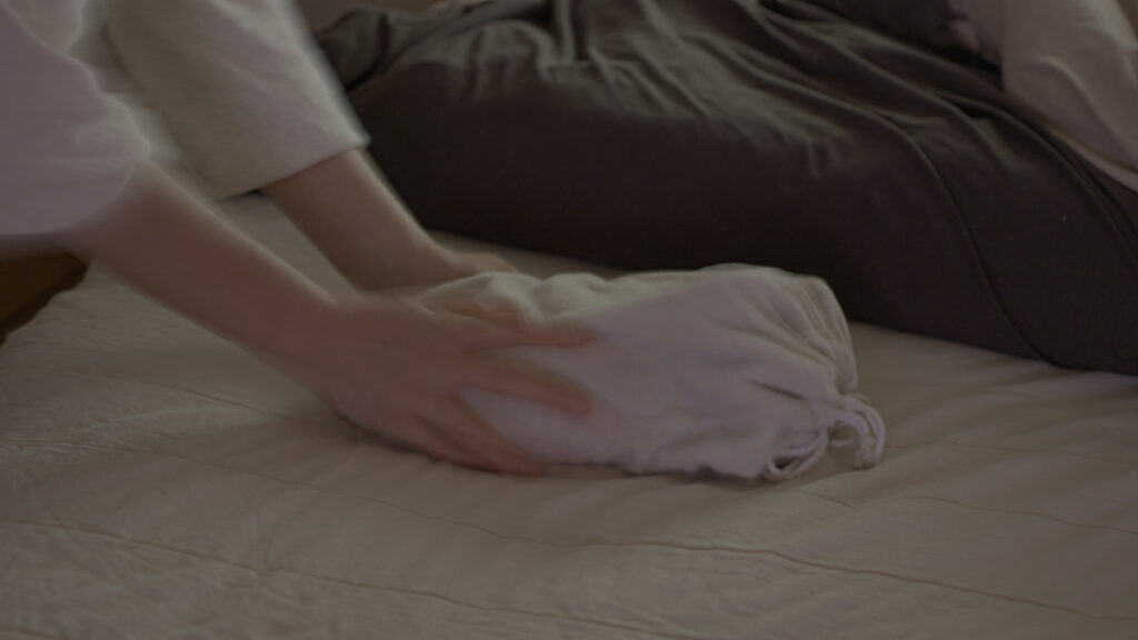 夜、布団の足元にマルカの金属製湯たんぽをそっと置き、朝まで続くやさしいぬくもりの準備をしている様子。布団の中で温かさが広がるイメージが伝わるシーン