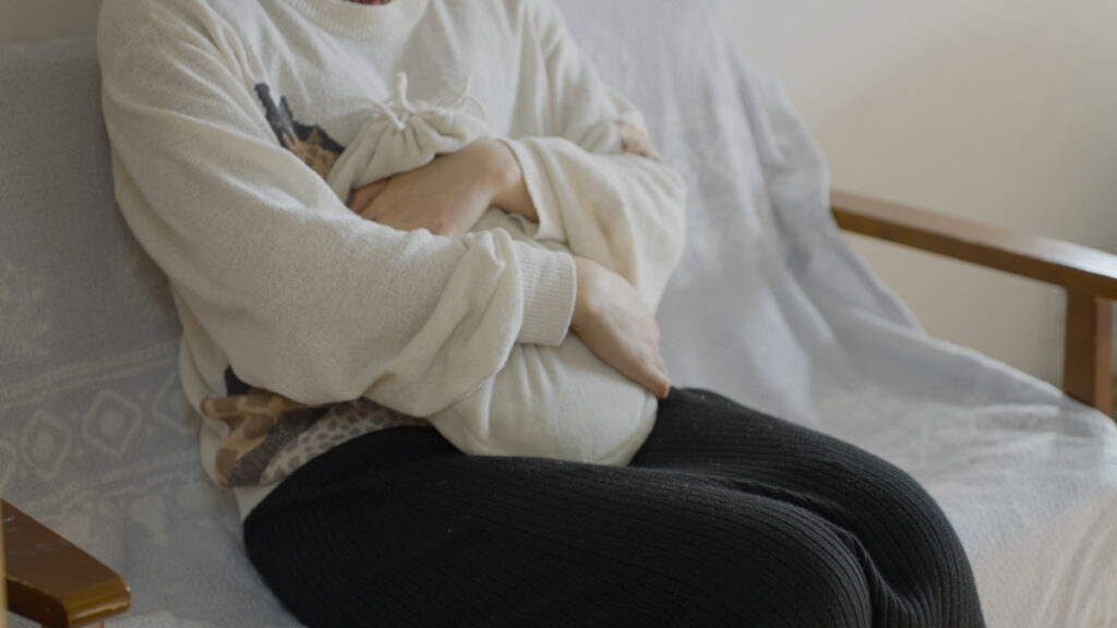 昼間のリビングで、マルカの金属製湯たんぽを膝の上で抱きかかえ、手で包みながら体の中心までじんわり温かさを感じてくつろいでいる様子